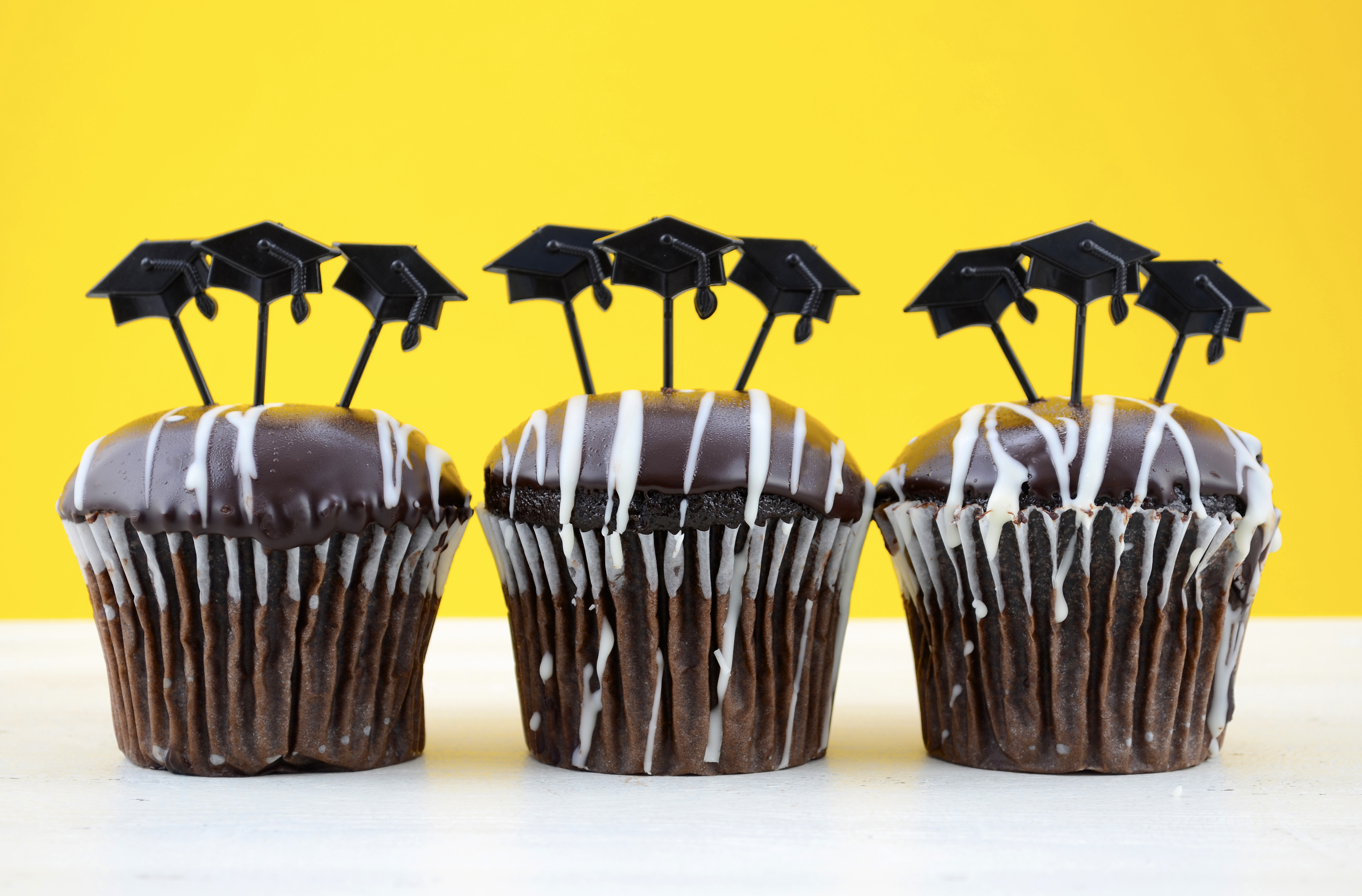 Happy Graduation Day party chocolate cupcakes with graduation cap hat topper decorations, in yellow, black and white party theme.